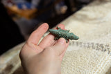 Small bronze crocodile pendant with green patina held in hand for scale.