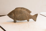 Three-quarter view of the vintage fish sculpture showing its carved scales and earthy patina.
