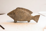 Vintage African fish sculpture showing its carved scales and weathered, earthen patina.