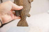 Close-up of the vintage fish sculpture's carved tail and raised, textured scales.