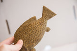 Textured scales and carved fins of the vintage African fish sculpture, held by a hand.