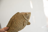 Angled profile view of the vintage fish sculpture's head, showing its textured scales and round eye.