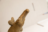 The textured, aged head of a vintage African crocodile sculpture viewed from below.