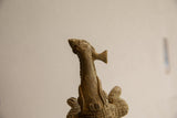 Close-up detail of the vintage crocodile sculpture's head holding a fish vertically.