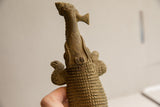 Upward view of the vintage crocodile sculpture, detailing its textured body and the fish in its mouth.