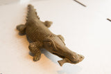 High-angle view of the vintage crocodile sculpture's textured head with a fish held in its mouth.