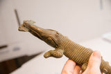 A hand holds the vintage crocodile sculpture, showing its textured bronze body and head.
