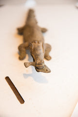 High-angle focus on the carved head of an African crocodile sculpture holding a fish.