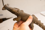 Detail of the vintage crocodile sculpture's head showing the fish in its mouth and carved body texture.