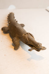 Low-angle view of the vintage crocodile sculpture's snout holding a small fish.
