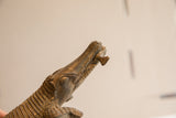 Close-up of the vintage crocodile's snout holding a small fish, showing aged patina.