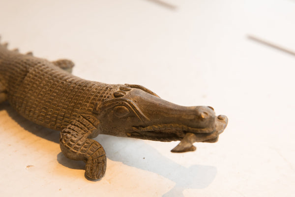 The carved head and expressive eye of the vintage crocodile sculpture holding a fish.