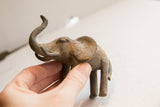 Vintage elephant sculpture with an aged patina held in hand for scale.