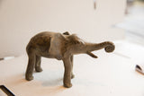 Side profile of a handmade elephant sculpture showing its rustic texture and raised trunk.