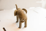 Handmade elephant sculpture seen from behind, showing its rustic texture and curled tail.