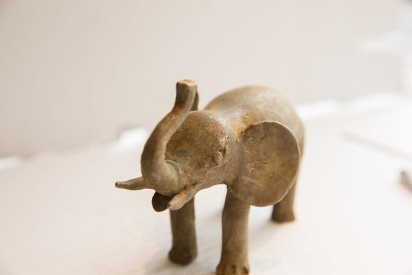 Angled profile of a vintage African elephant sculpture showing its textured body and upward-curling trunk.