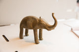 The textured, handmade form of a vintage elephant sculpture with its trunk up.