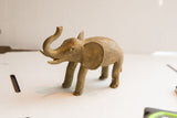 Side profile of a vintage elephant sculpture showing its rustic handmade texture and raised trunk.