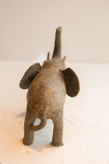 The textured, handmade back of a vintage elephant sculpture with its trunk raised high.