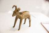 The rustic, handmade form of a vintage African ram sculpture, seen from a side angle.