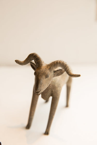 Vintage African ram sculpture seen head-on, highlighting its rustic texture and horns.