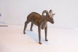 Angled view of the handmade African ram sculpture showing its textured body and curled horns.