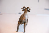 The back of a handmade ram sculpture with a textured spine and curled tail.