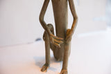 A close-up of the slender arms and detailed hands of the sitting monkey sculpture.