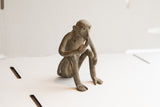 Side profile of a vintage African monkey sculpture in a thoughtful, seated posture.