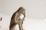 Side profile close-up of the vintage monkey figurine highlighting its weathered, handmade surface.