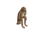 Vintage handmade African monkey figurine with a rustic brown patina, posed eating a banana.