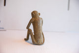 Rear view of a vintage African monkey figurine showing its seated posture and textured surface.