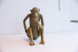 The vintage African monkey figurine's aged patina and thoughtful pose from a side angle.