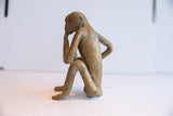 Side profile of the sitting monkey figurine, showing its pensive pose and aged texture.