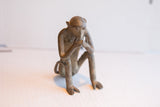 Side view of the vintage African monkey sculpture, showing its thoughtful pose and aged patina.