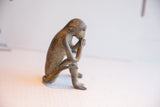 Profile view of a vintage monkey figurine highlighting its pensive posture and textured finish.