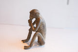 Profile view of the sitting monkey figurine, showing its thoughtful posture and aged patina.