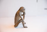 A vintage African monkey sculpture viewed from the side in a thoughtful, seated pose.