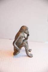 Side view of a vintage monkey figurine showing its contemplative pose and aged patina.