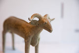 Close view of the vintage African ram sculpture's head, detailing the earthy patina and curved horns.