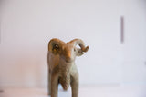 The textured, aged patina on the face and large curled horns of a vintage ram sculpture.