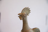 Vintage African rooster sculpture's head, showing spiral eye, ribbed neck, and verdigris patina.
