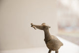 Profile view of the textured head of an African bird sculpture holding a fish.