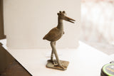 Profile view of a vintage African bird sculpture showing its textured body and etched wing detail.
