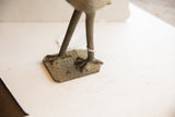 Aged patina and handmade texture on the sculpture's feet and square base.