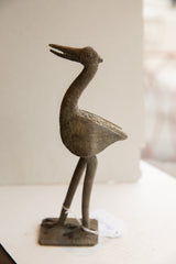 Profile of a vintage African bird sculpture with a long neck and textured, aged finish.