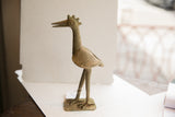 Side profile of a handmade African bird sculpture showing its crown and aged patina.