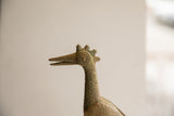 Profile view of a vintage bird sculpture's head with a stylized spiral eye and crest.