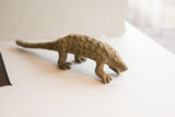 Profile view of a vintage pangolin sculpture showing its arched back and rustic, scaled texture.