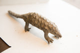Full profile view of a vintage pangolin sculpture highlighting its handmade scaled texture.